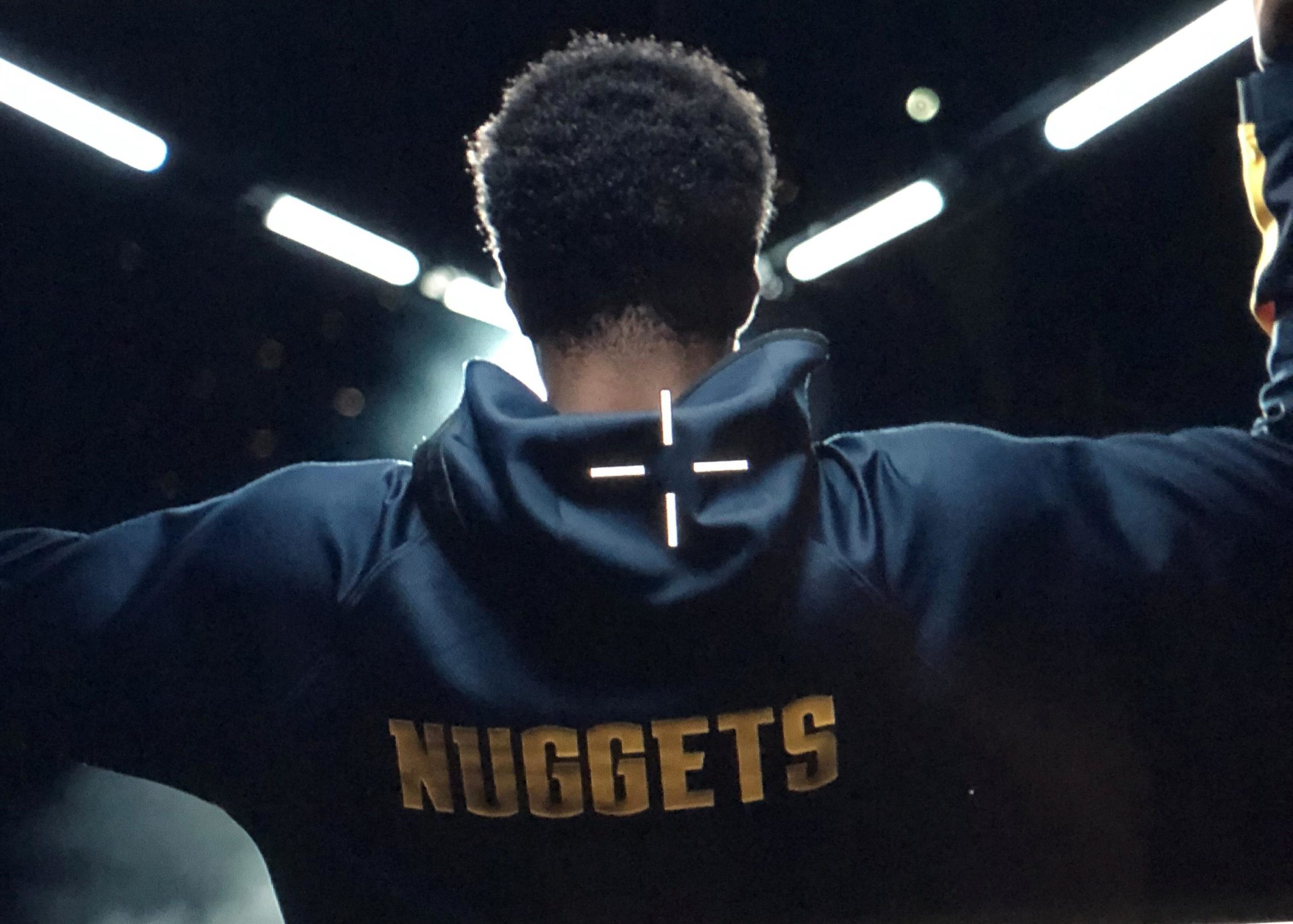 Backlit athlete wearing a Denver Nuggets jacket under dramatic lighting on a production set